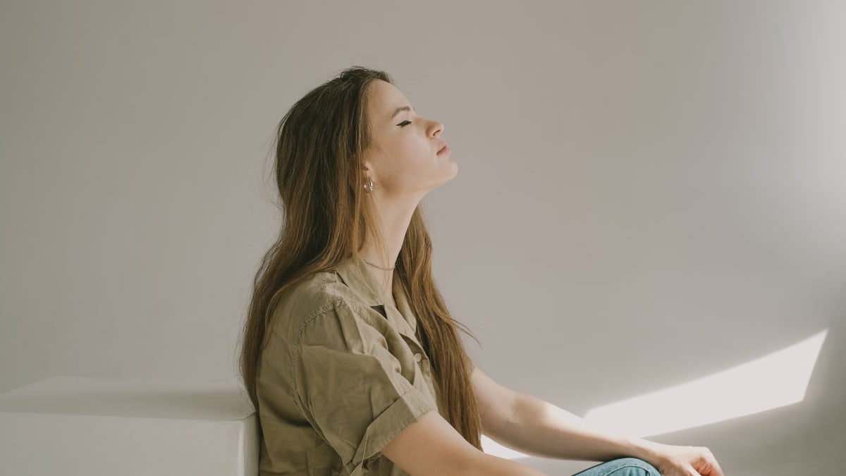 Side profile of a young woman sitting indoors, lost in thought with eyes closed.